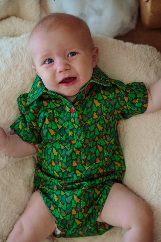 Baby wearing a green patterned outfit lying on a beige blanket