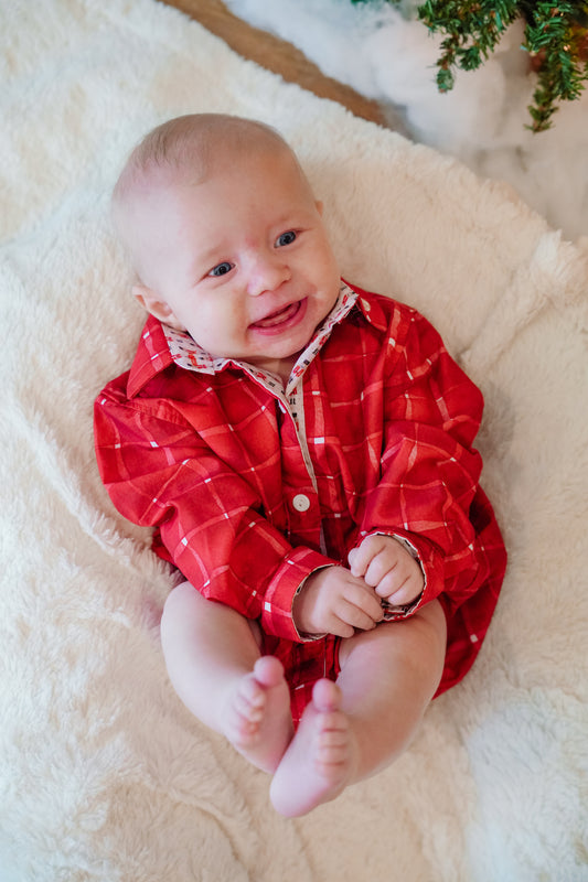 Baby wearing a red plaid outfit on a white blanket