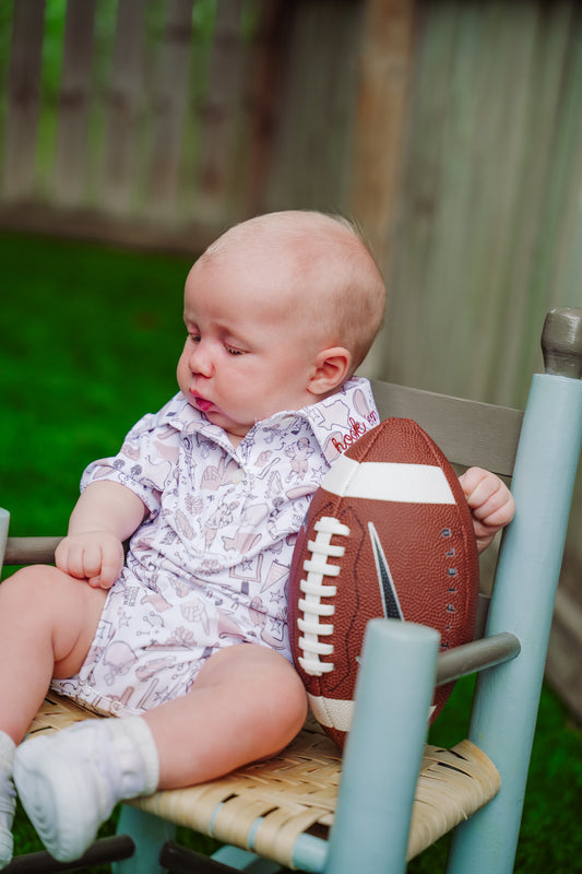 Baby wearing the Gameday Polo Bodysuit sitting beside a football.