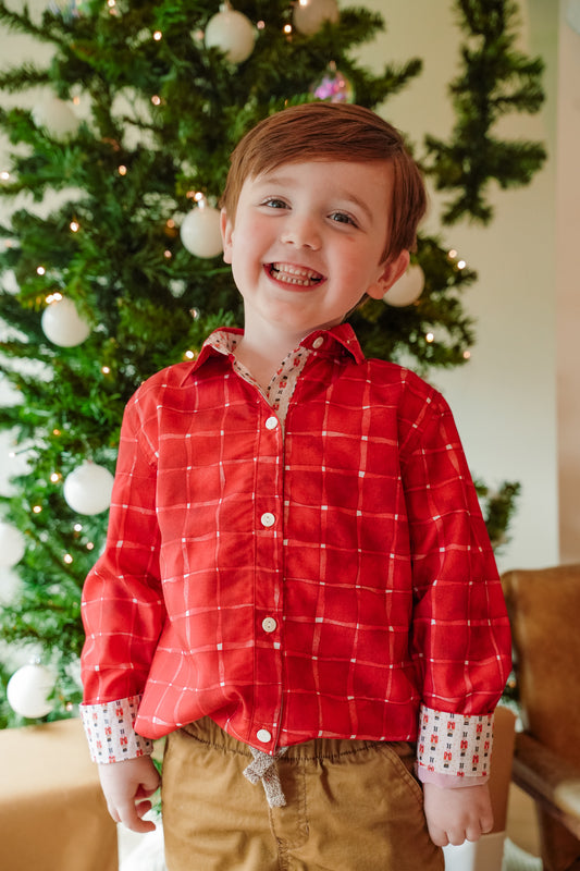 Child wearing a red plaid shirt in front of a decorated Christmas tree
