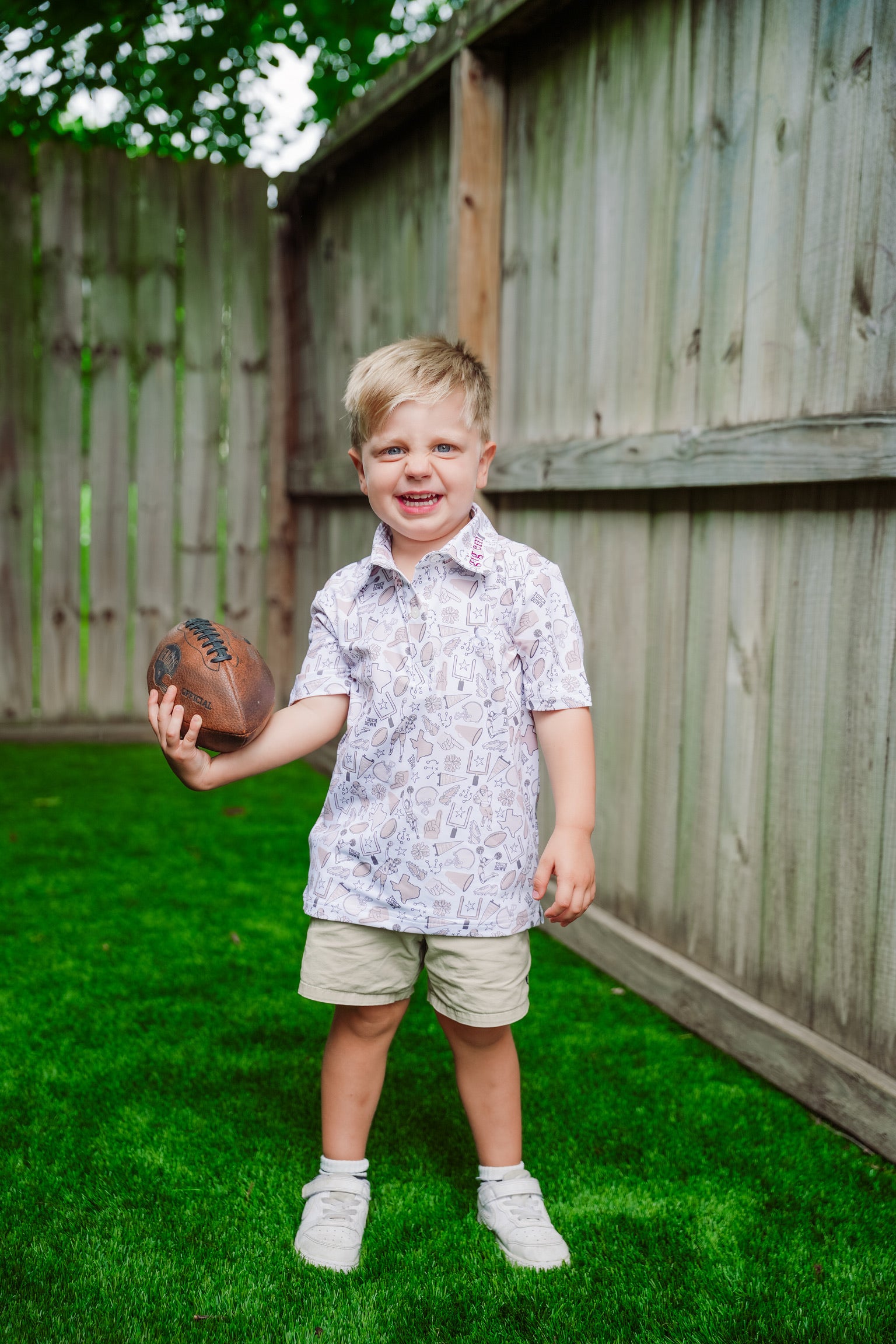 Child holding a football in gameday polo in a backyard setting