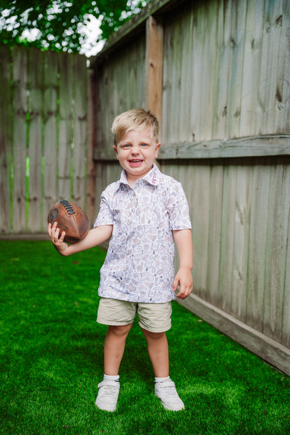Child holding a football in gameday polo in a backyard setting