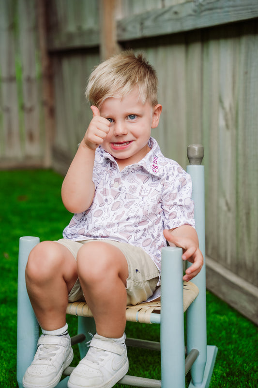 Young boy giving a thumbs up while wearing a boys football polo shirt with a neutral gameday print and embroidered collar.