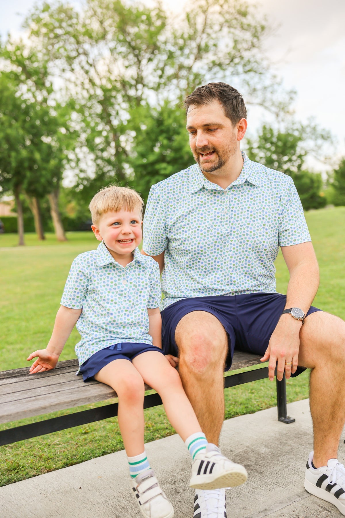 Father and son wearing matching Dapper Dog dog print polo shirts while sitting together outdoors.
