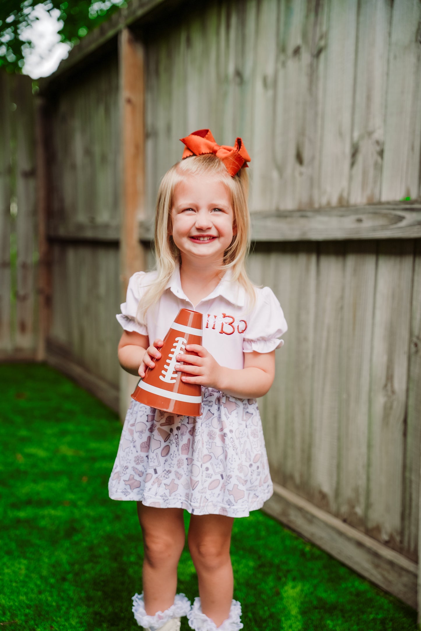 Young girl holding a toy cup with a football design, standing in a backyard.