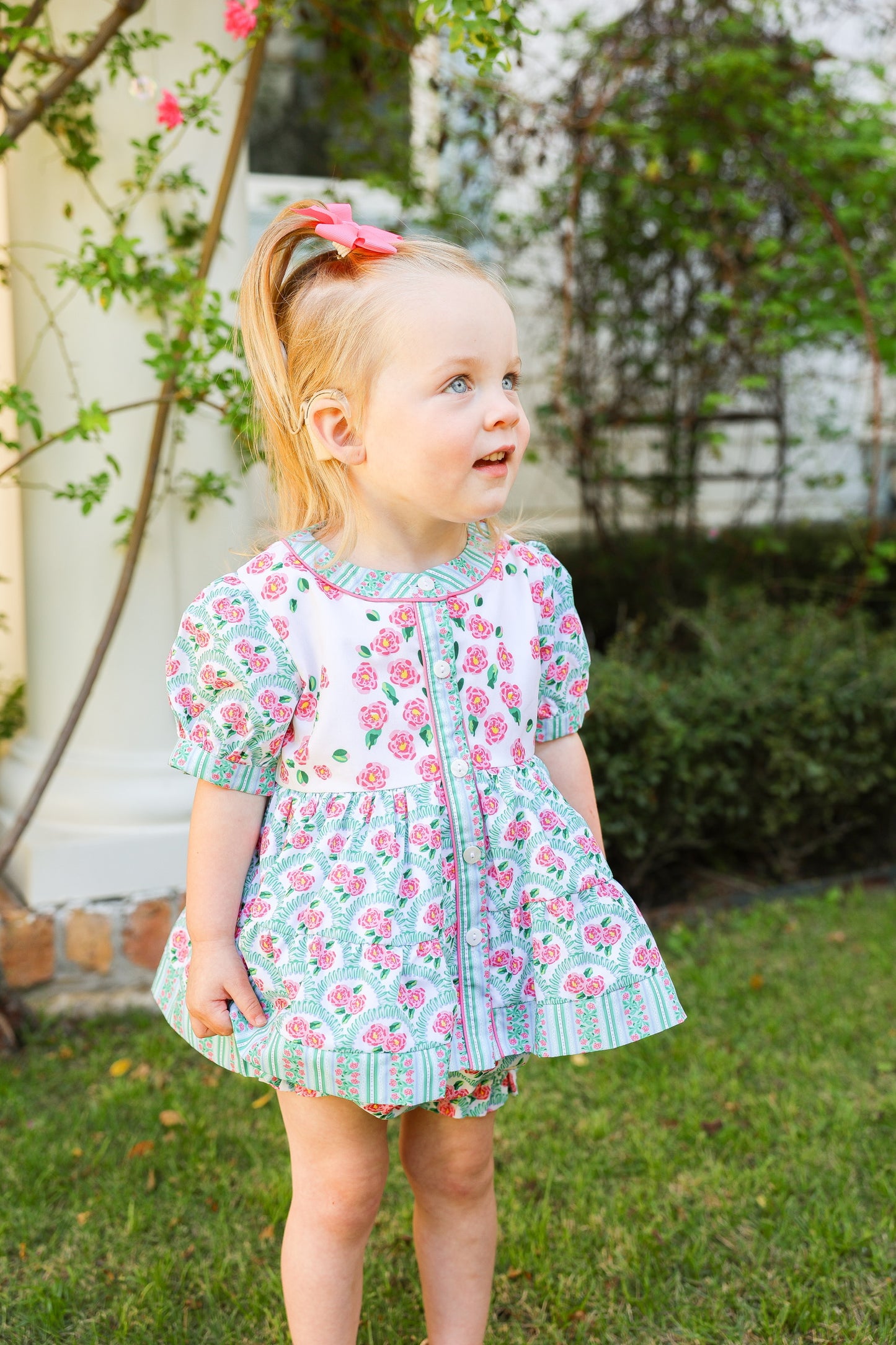 Young girl in a floral dress standing outdoors with greenery in the background