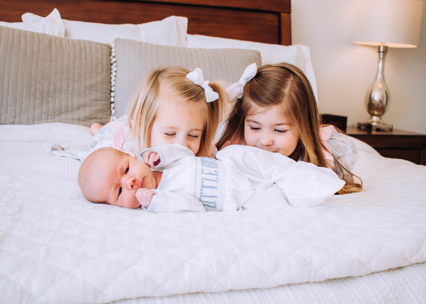 Two young girls holding a newborn baby on a bed.