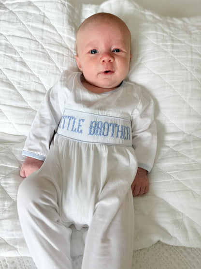 Newborn baby wearing Sawyer + Spade Little Brother Smocked Footie with blue hand-smocked embroidery lying on a white quilt