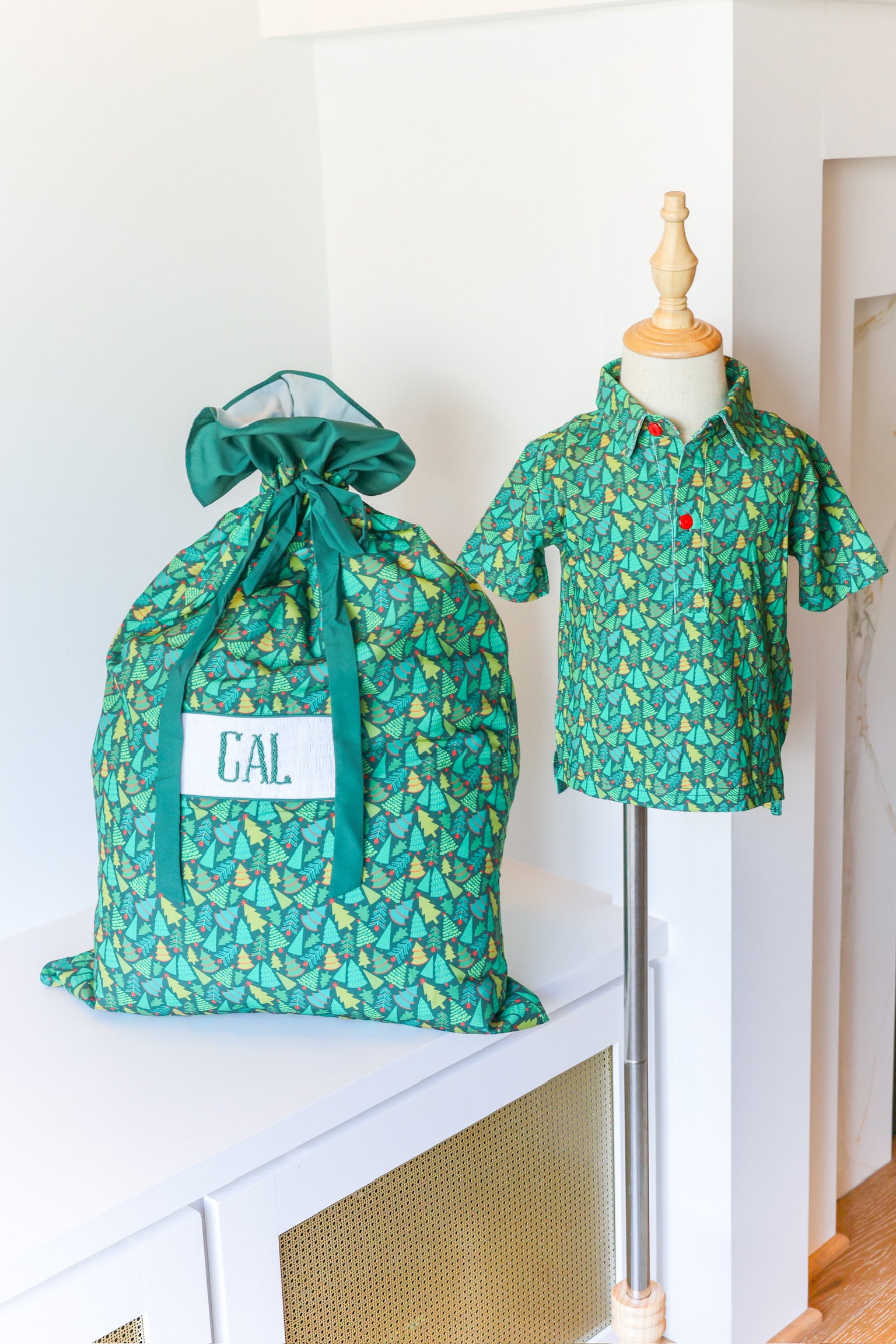 A green patterned drawstring storage bag with a white label reading 'CAL.' sits on a white cabinet beside a mannequin wearing a matching short-sleeve collared shirt.