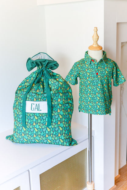 A green patterned drawstring storage bag with a white label reading 'CAL.' sits on a white cabinet beside a mannequin wearing a matching short-sleeve collared shirt.