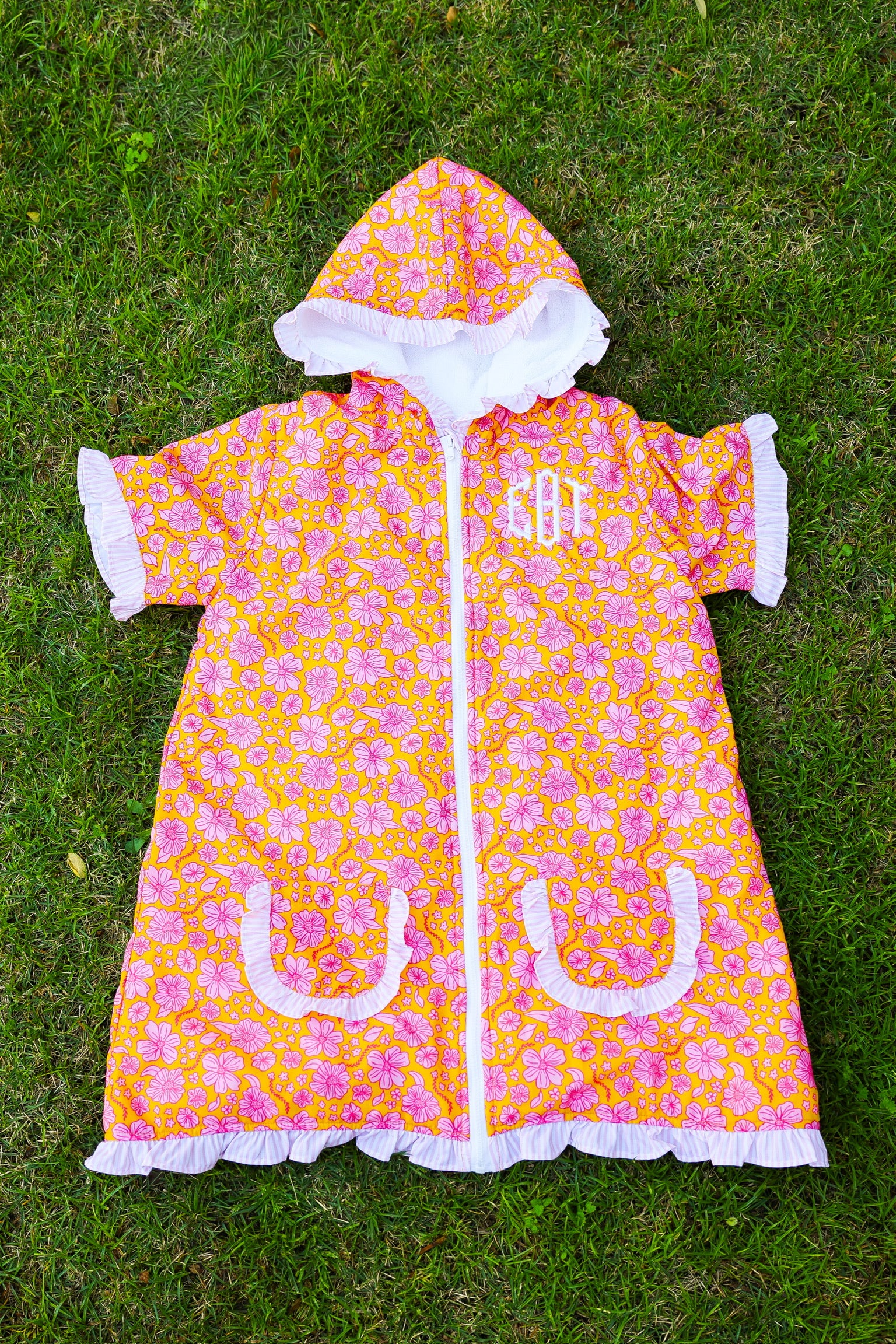 Pink floral kids hooded towel poncho with ruffle trim and front pockets on grass