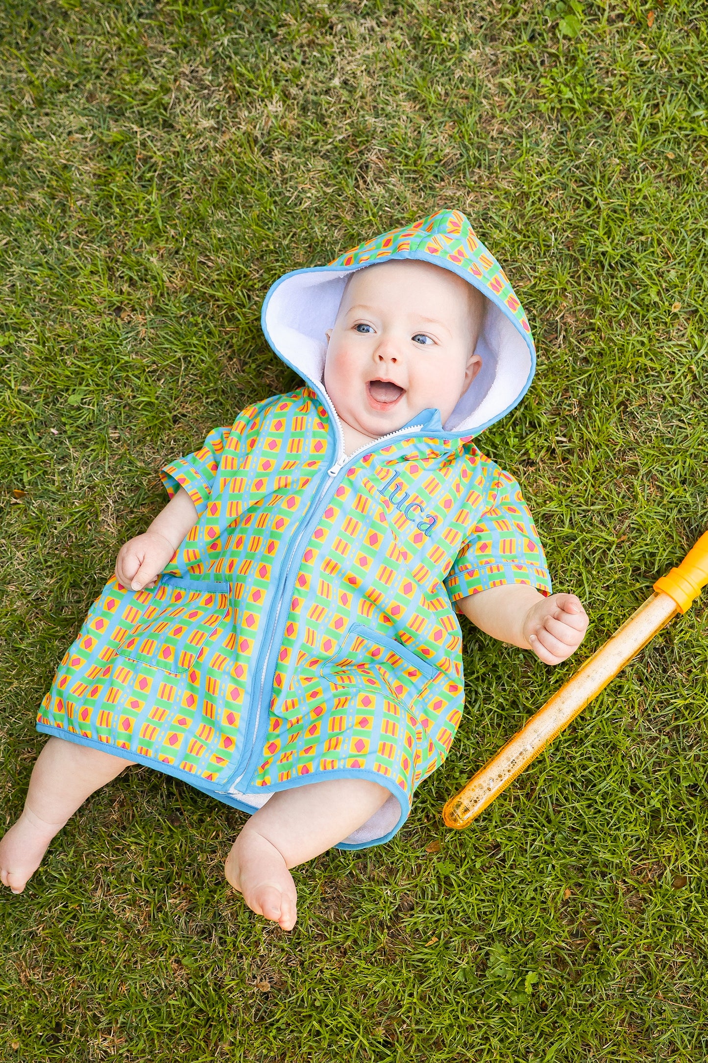 Baby wearing the Retro Splash hooded towel poncho while relaxing outdoors after swimming