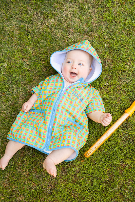 Baby wearing the Retro Splash hooded towel poncho while relaxing outdoors after swimming