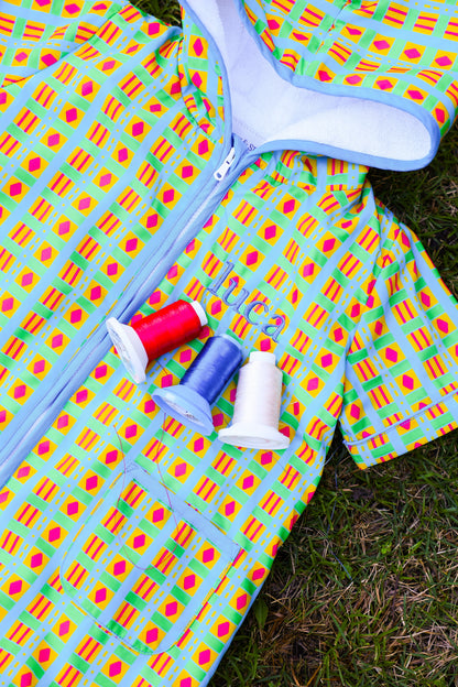 Colorful patterned fabric with spools of thread on a grassy background